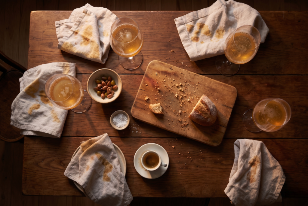 Social bonding through food — the remains of a shared meal with bread crumbs, wine glasses and linen napkins on wood. 