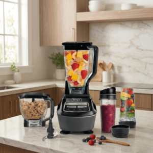 Ninja Kitchen System blender on a modern kitchen counter with a pitcher full of mixed fruit, smoothie cups, food processor bowl, and blending accessories.