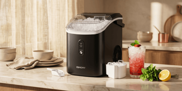 Compact matte black countertop ice maker on a pale marble surface in a sunlit kitchen, with a glass of pellet ice, fresh mint, and lemon accents in warm golden hour light.