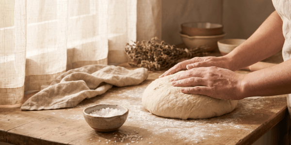 Hands kneading soft bread dough on a wooden board — practicing mindfulness in the kitchen on a quiet flour-dusted morning