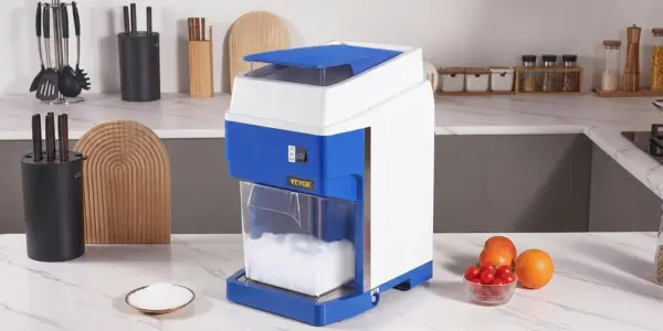 A VEVOR commercial electric snow cone machine and ice shaver on a modern white marble kitchen countertop, filled with freshly shaved fluffy snow.