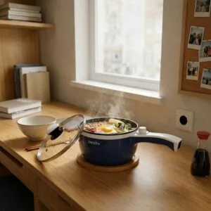 Navy non-stick electric pot simmering ramen on a small dorm desk